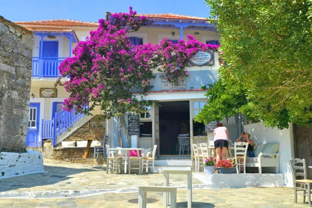 A whitewashed cafe with blue doors surrounded by purple bougainvillea