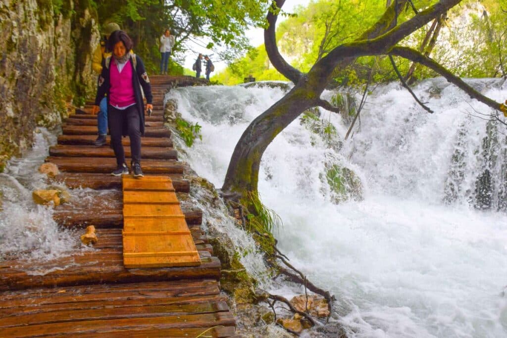 A women carefully navigates a wooden path as water rushes around it at Plitvice Lakes National Park in Croatia
