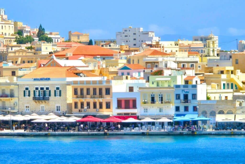 A row of waterfront cafes in Syros Greece with colorful umbrellas over outdoor seating